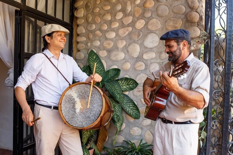 Two men playing instruments outside by a stone wall, enjoying music together.